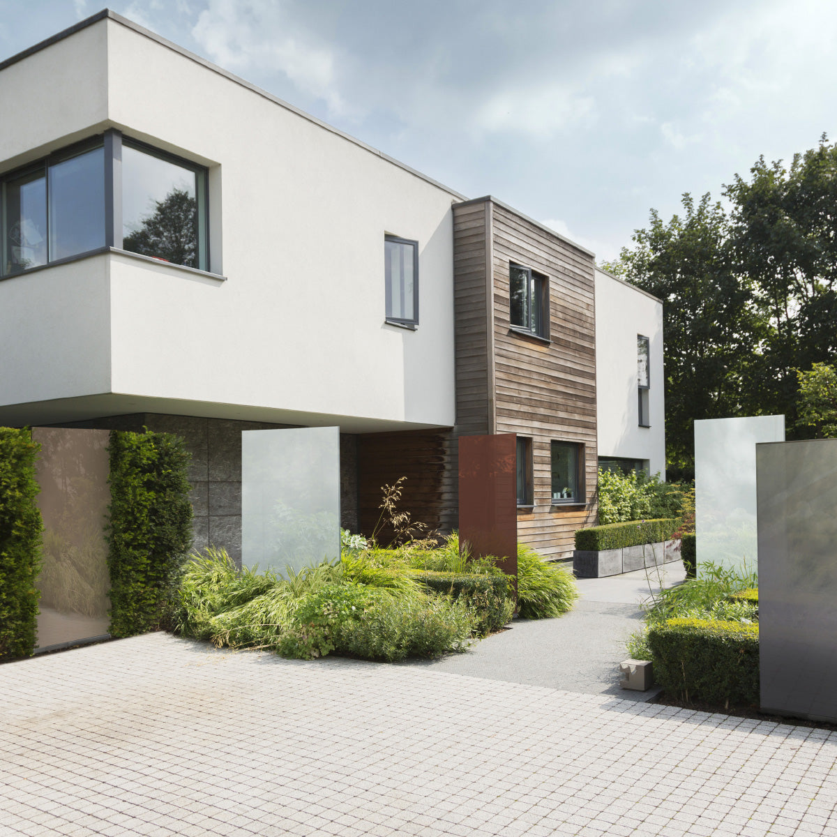 Fünf KNUMOX Glasdesign Elemente stehen vor einem modernen Haus. Zwei der Elemente sind weiß, zwei sind beige-braun und eines ist grau.