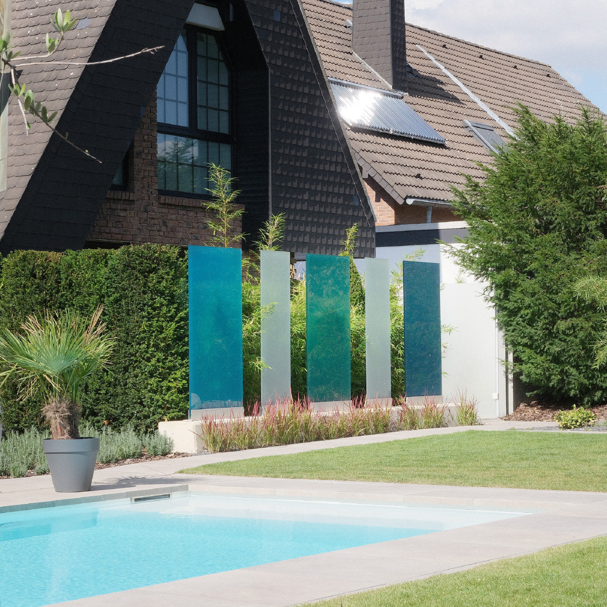 Drei blaue und zwei weiße Sichtschutzelemente der Firma KNUMOX stehen neben einem Pool vor einem Haus.