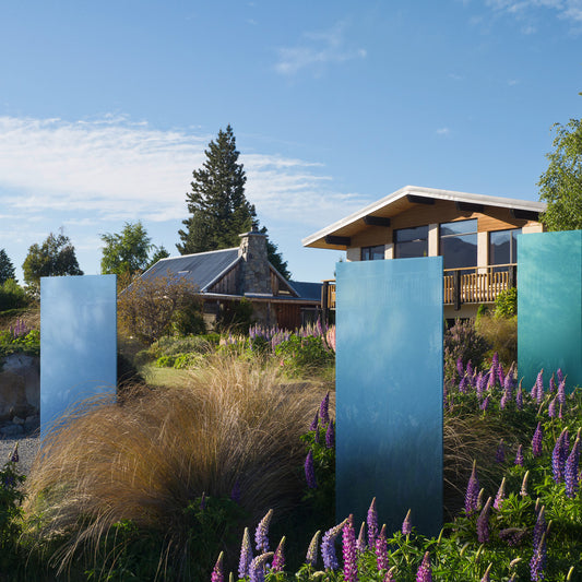 Drei blaue KNUMOX Glasdesign Elemente stehen in einem Garten mit üppiger Bepflanzung. 