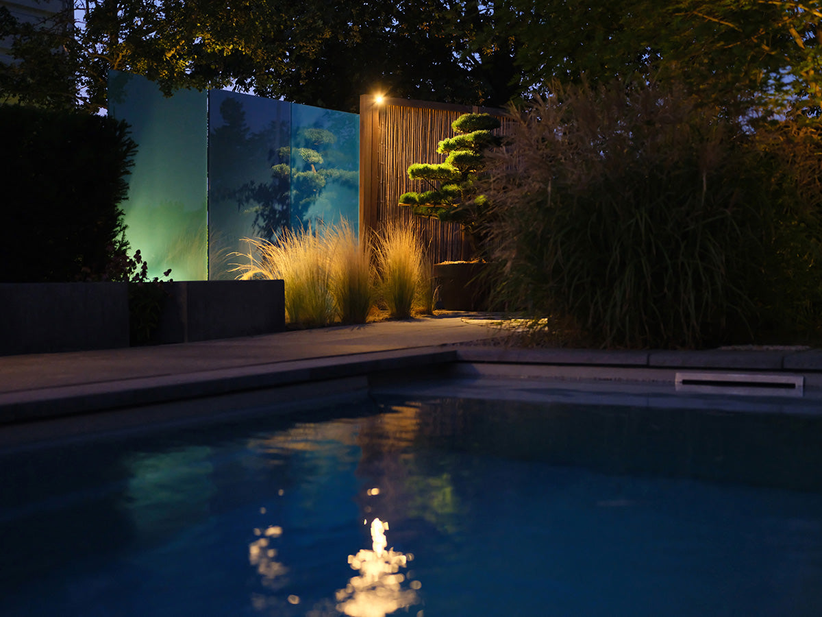 Garten mit Pool und beleuchteten Glaselementen als Sichtschutz bei Nacht